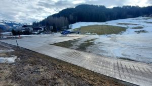 Lądowisko dla helikopterów na tle górskiego krajobrazu, z resztkami śniegu i zieloną trawą.