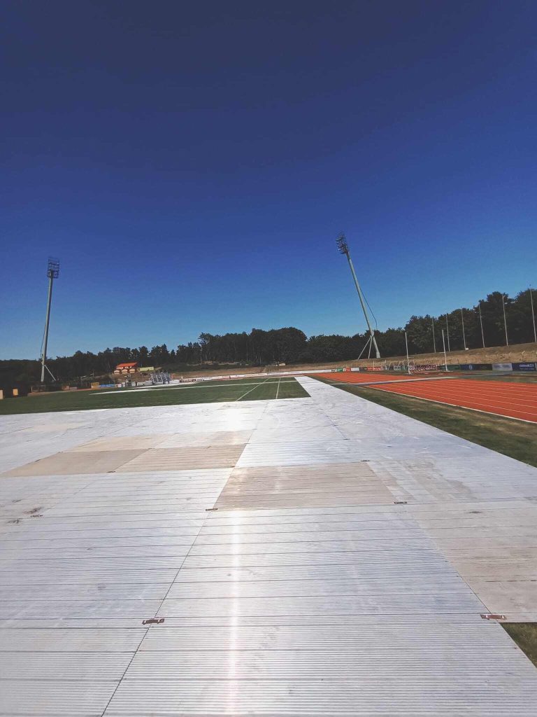 Widok na stadion z torami biegowymi, z płaską powierzchnią i jasnym niebem w tle.