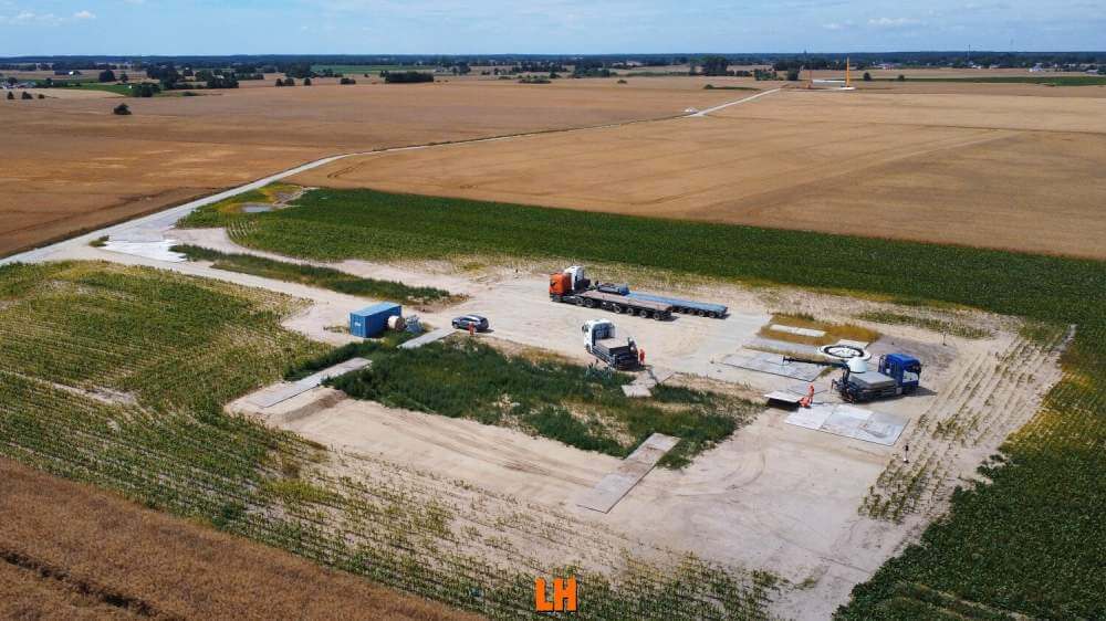 Widok na plac budowy lub parking w otoczeniu pól uprawnych, z pojazdami i maszynami.