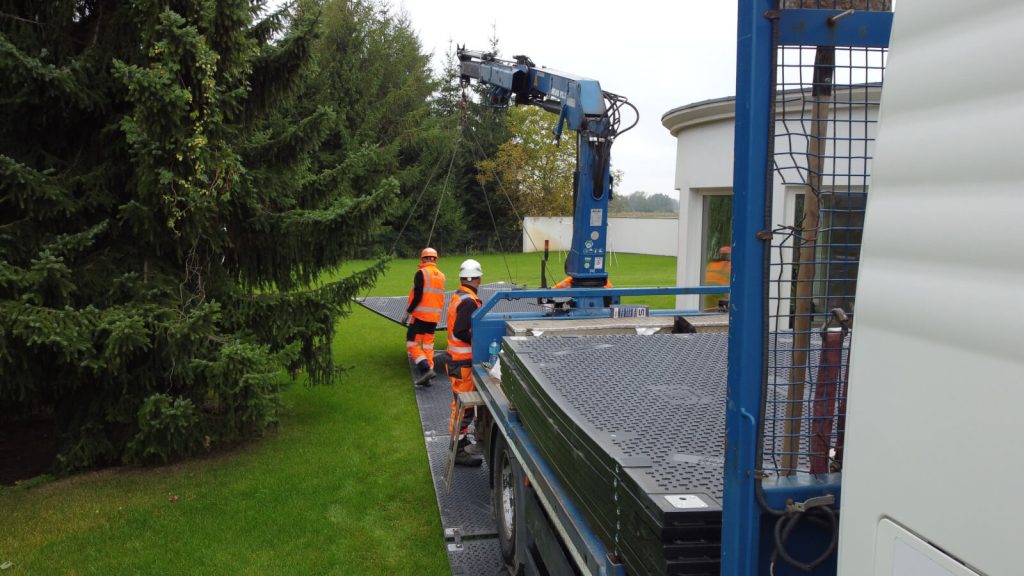 Pracownicy w odblaskowych kamizelkach montują elementy budowlane przy użyciu maszyny dźwigowej.