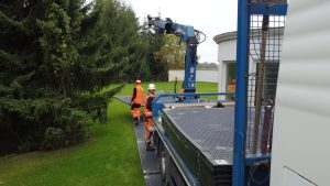 Pracownicy w odblaskowych kamizelkach montują elementy budowlane przy użyciu maszyny dźwigowej.