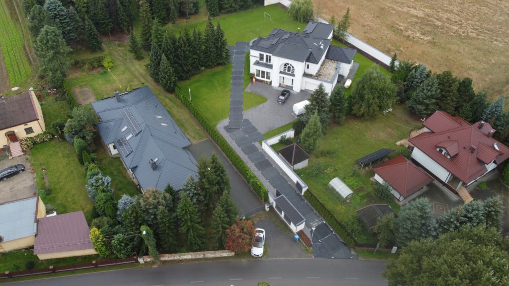 Widok z góry na osiedle domów jednorodzinnych, w tym dużą willę z tarasem i zielonym otoczeniem.