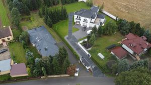 Widok z góry na osiedle domów jednorodzinnych, w tym dużą willę z tarasem i zielonym otoczeniem.
