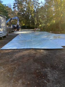 Metalowa platforma leży na ziemi w lesie, obok widoczny ciężki sprzęt budowlany i znak ostrzegawczy.