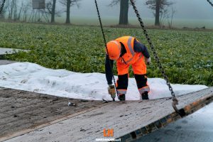 Pracownik w pomarańczowej odzieży roboczej demontuje panele na polu w mglistym otoczeniu.