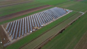 Widok z lotu ptaka na farmę słoneczną z panelami słonecznymi na zielonym polu. W tle widać maszyny budowlane.
