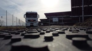 Transport ciężarowy na drodze w pobliżu paneli słonecznych, z widokiem na słoneczne niebo.