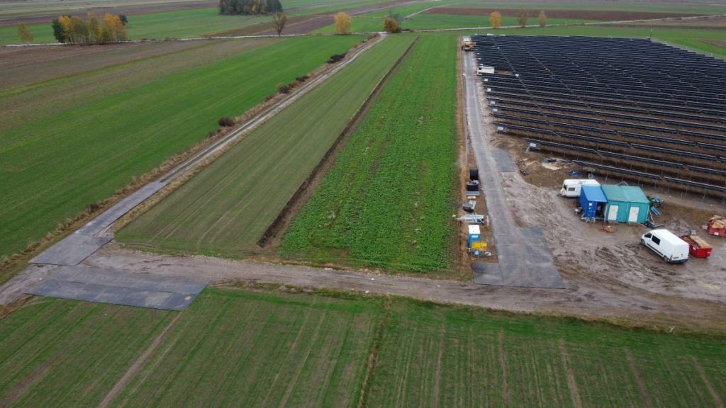 Na obrazie widać rozległe pola uprawne, fragment gruntu przygotowanego pod nasadzenia oraz pole z panelami słonecznymi.