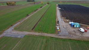 Na obrazie widać rozległe pola uprawne, fragment gruntu przygotowanego pod nasadzenia oraz pole z panelami słonecznymi.