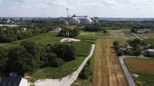 Widok z lotu ptaka na tereny zielone, pola uprawne i silosy w oddali, przy gęstej roślinności.