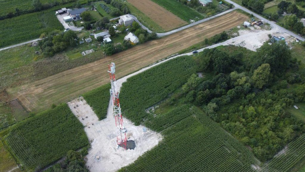 Widok z lotu ptaka na wieżę telekomunikacyjną otoczoną polami i domami.