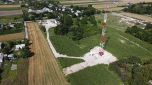 Wiejska sceneria z zielonymi polami, mnóstwem domów, a w centralnej części wieża telekomunikacyjna.